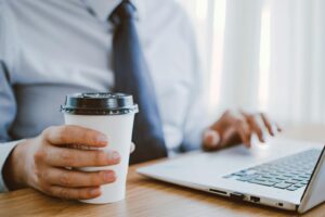 Professionnel travaillant à distance, savourant un café tout en utilisant un ordinateur portable à l'intérieur.