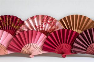 Une collection de plusieurs éventails de différentes nuances de rouge et de rose, dont plusieurs modèles de L’Éventail de Poche