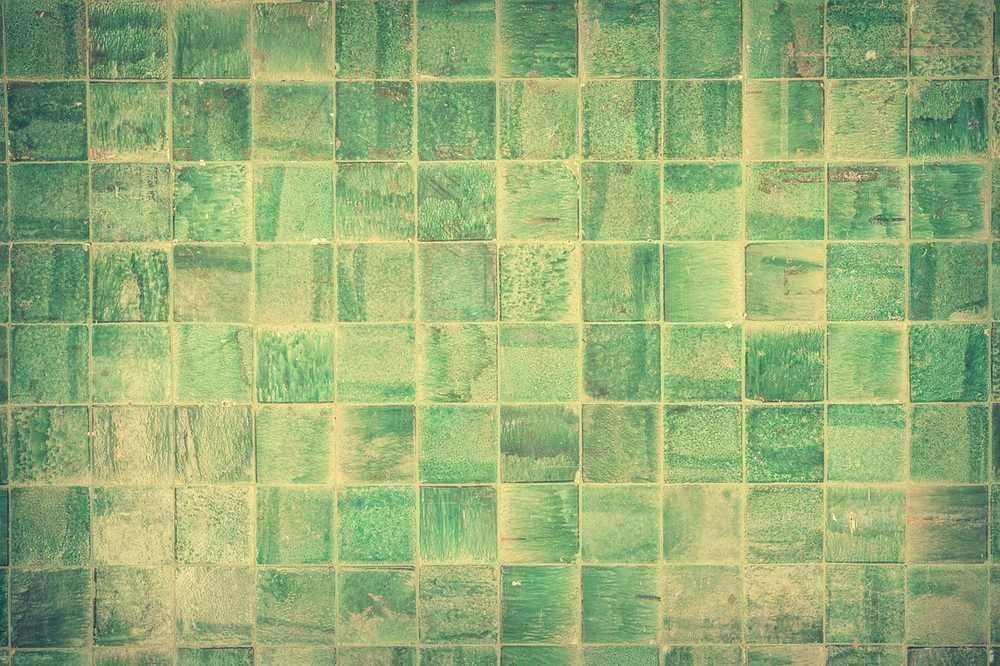 Carrelage vert usé recouvre un mur, teintes variées et légèrement ternies