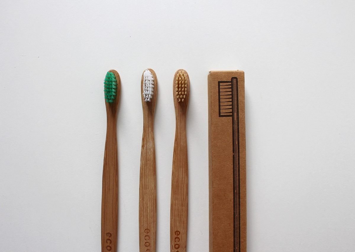 Trois brosses à dents en bambou et une boîte en carton sur fond blanc
