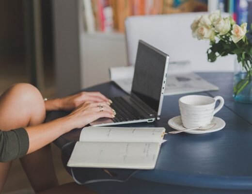 Une femme travaille sur ordinateur, note dans cahier, boit café près de fleurs